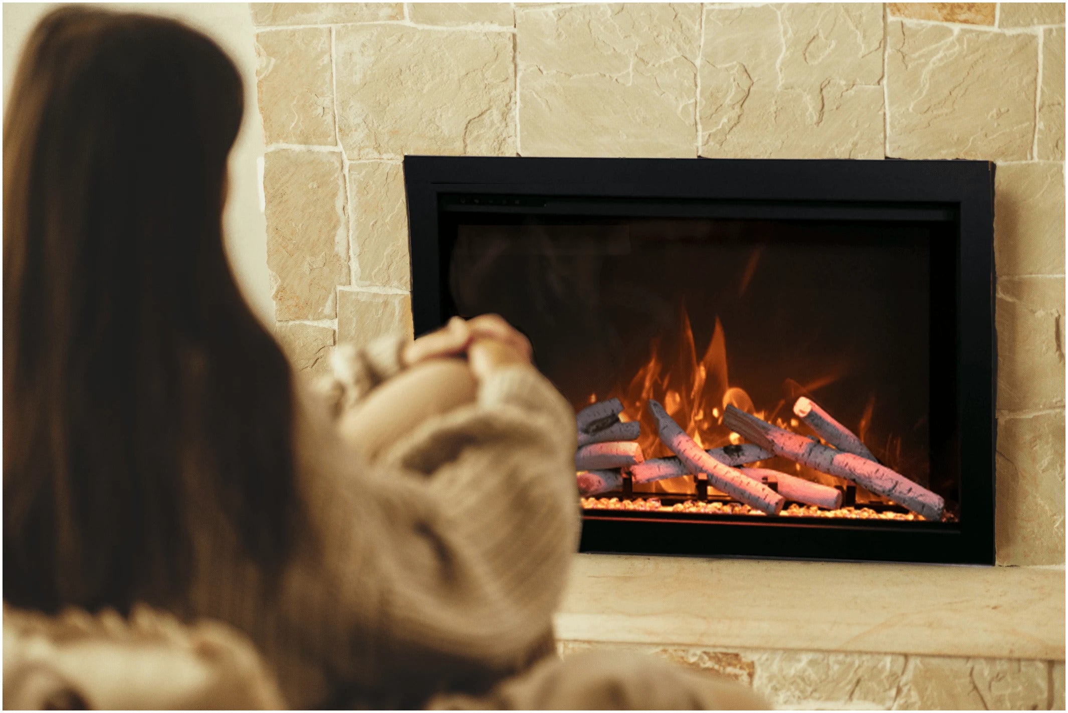 Amantii TRD-30-BESPOKE Electric Fireplace - Person wearing a sweater sitting in front of a fireplace with flames.
