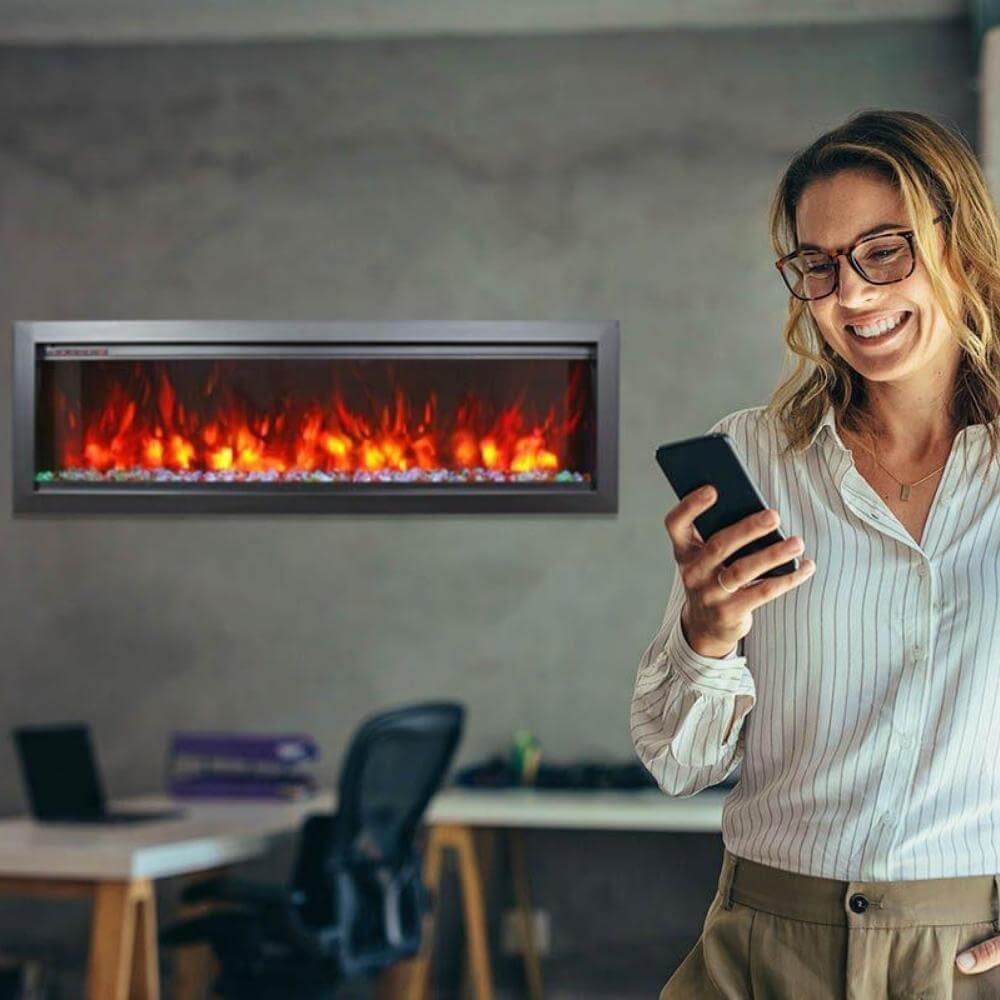 Amantii Symmetry Bespoke Electric Fireplace - A woman with a cell phone in hand admires a crackling fireplace
