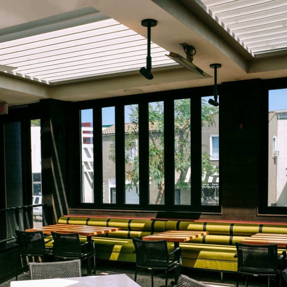 Interior of a modern commercial space with seating, featuring large windows and Bromic electric heater installation.