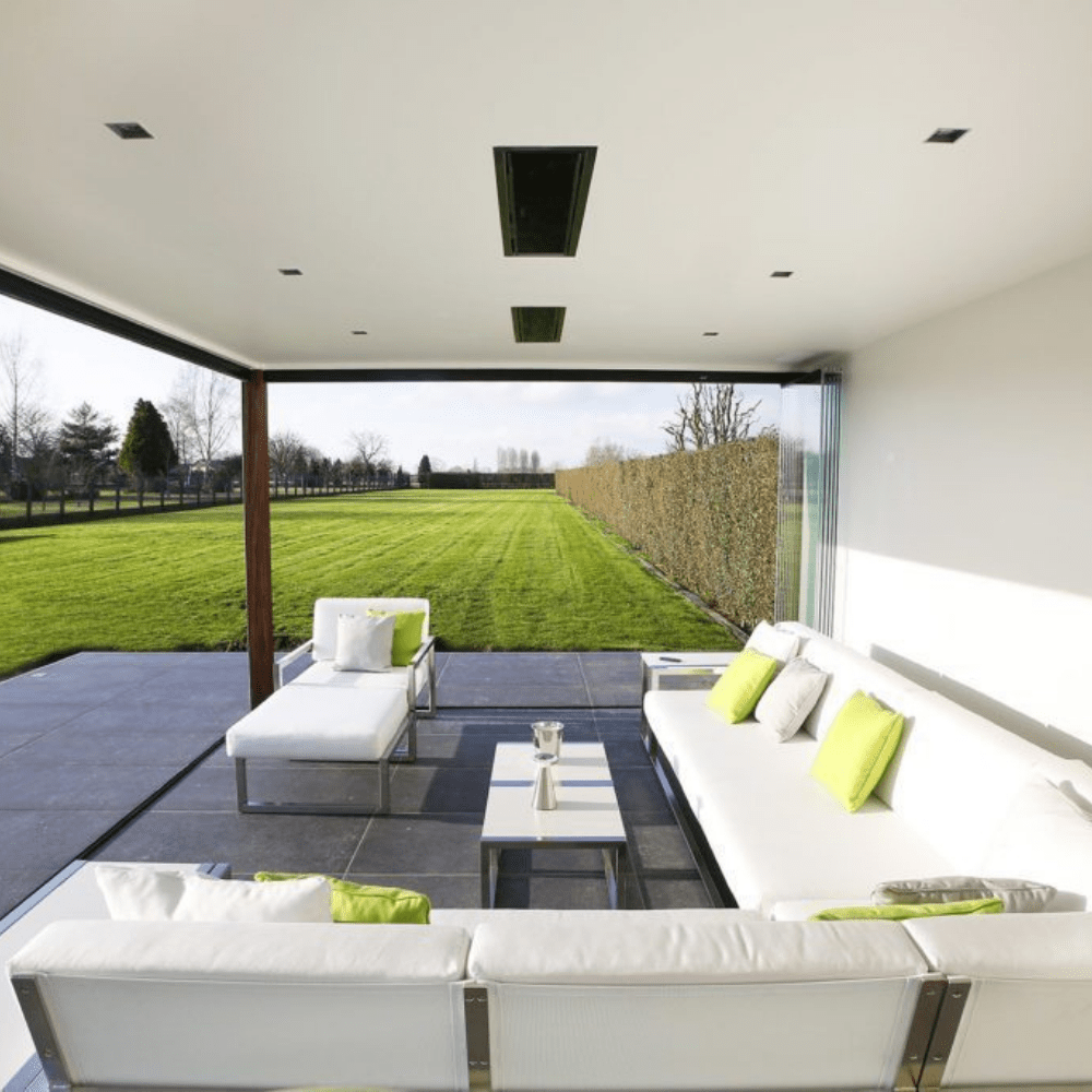 Modern outdoor lounge with white furniture and green accents overlooking a sunny garden.