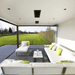 Modern outdoor lounge with white furniture and green accents overlooking a sunny garden.