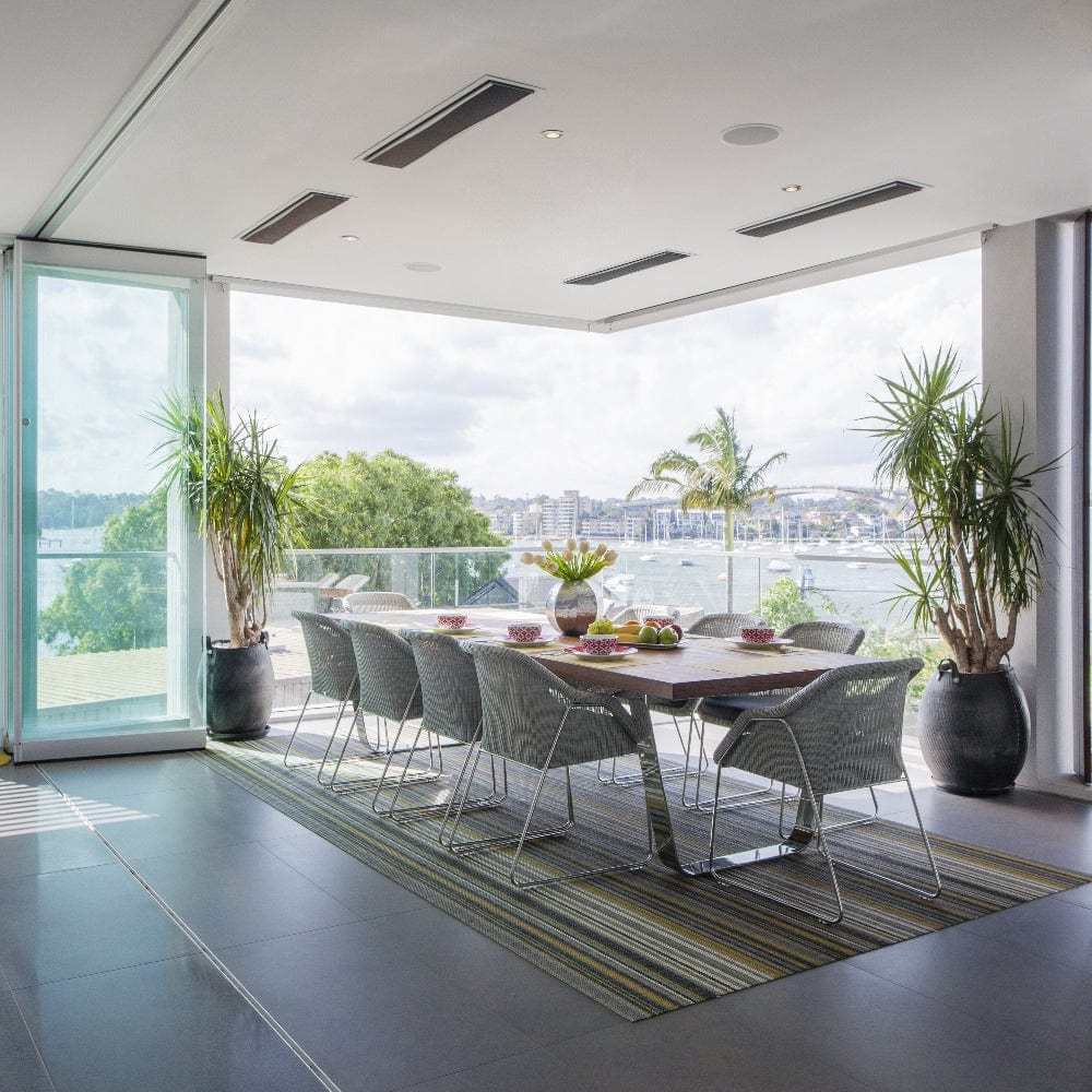 Elegant outdoor dining area with Bromic Platinum heaters, featuring a scenic view and stylish furnishings.