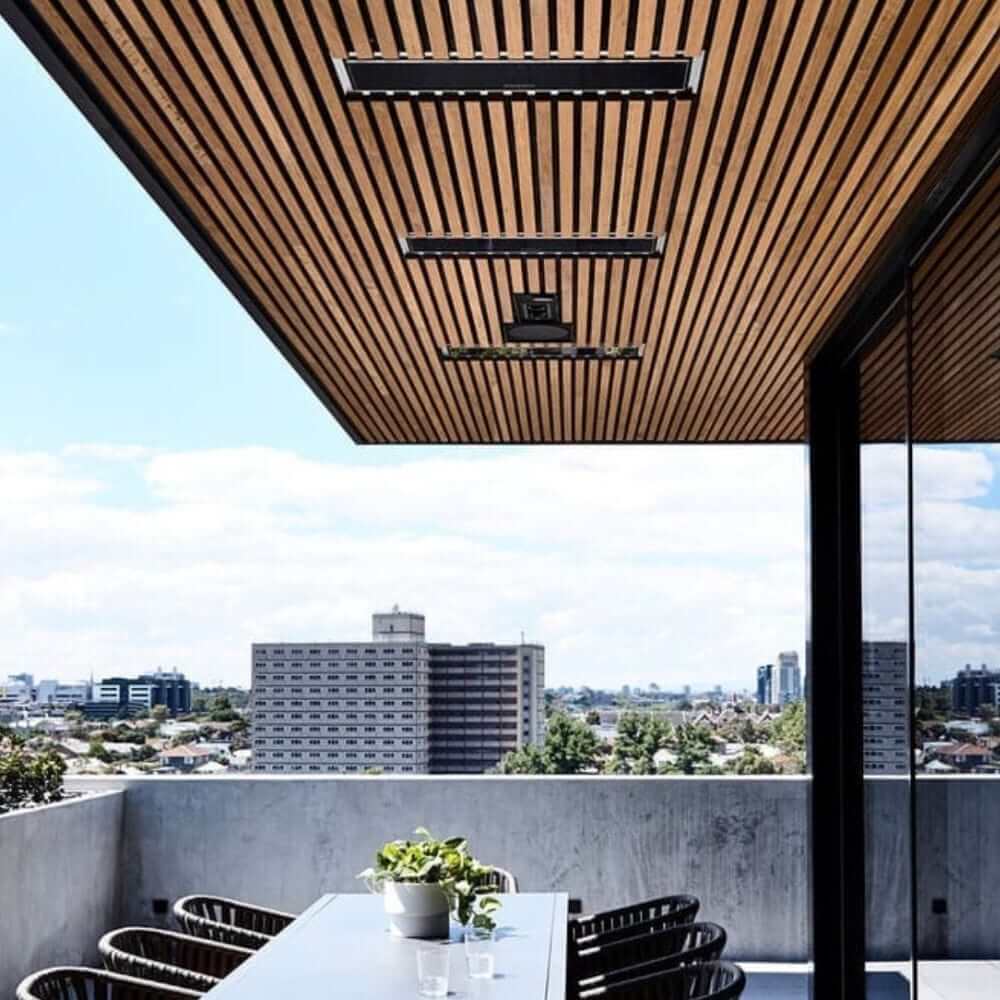 Stylish outdoor space featuring Bromic Platinum electric heaters mounted on a wooden ceiling with city view.