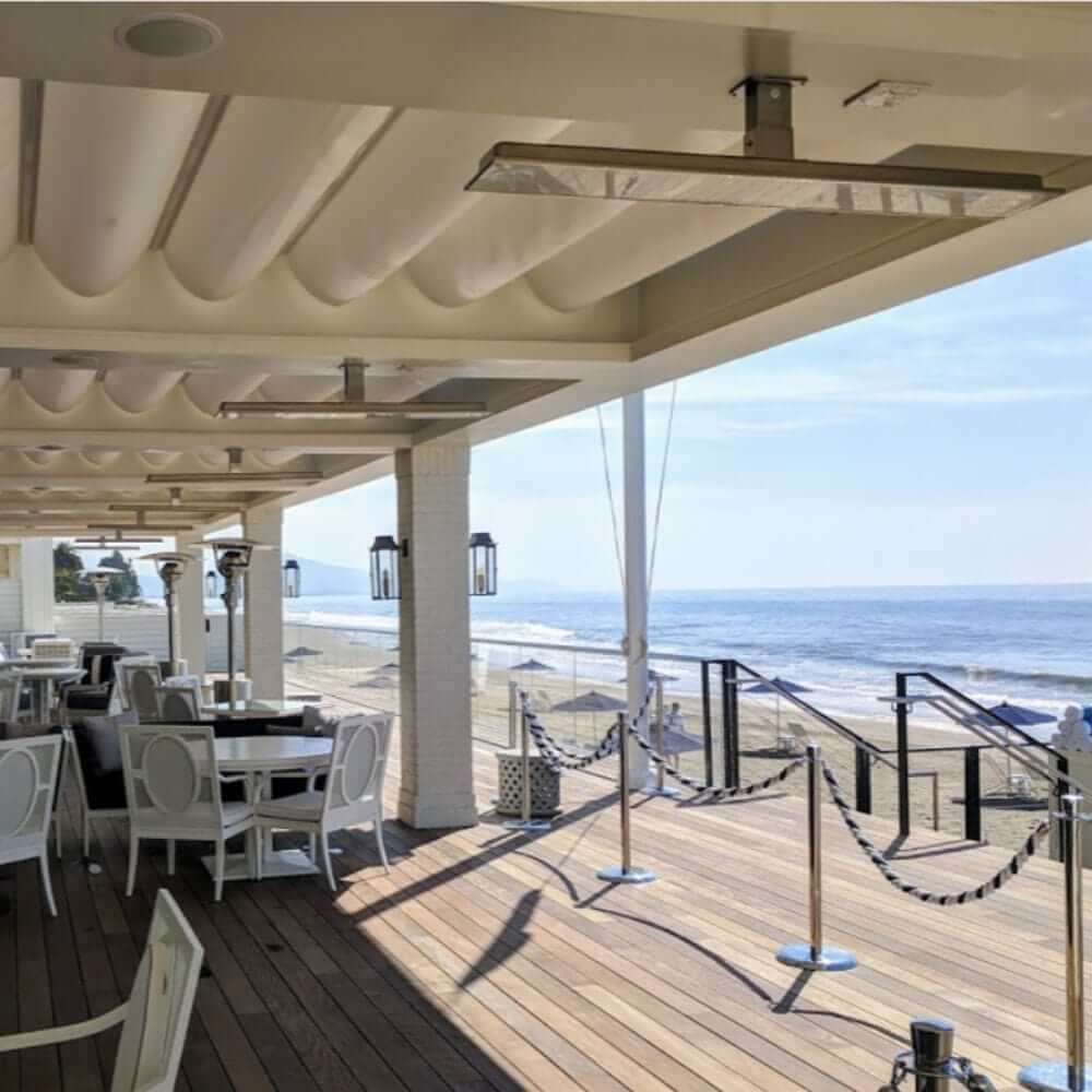 Stylish outdoor dining area featuring Bromic electric heaters with ocean view.