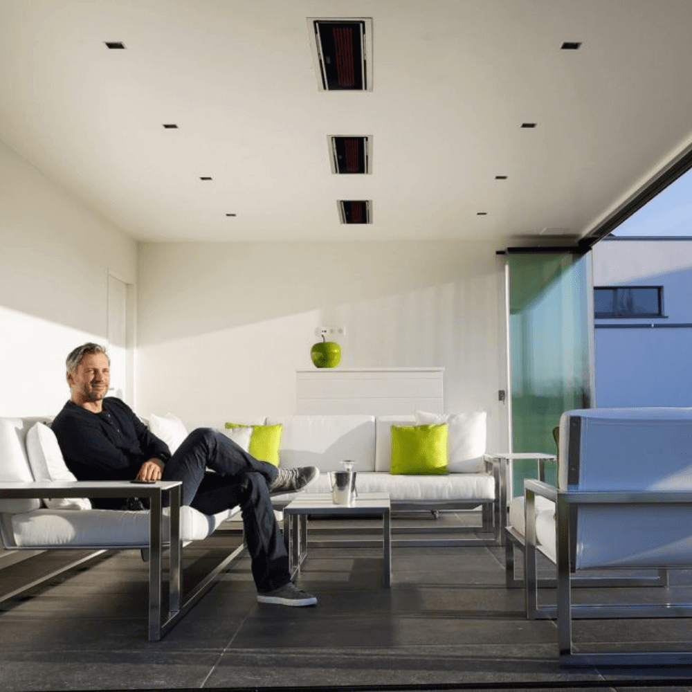 Modern indoor lounge with a man relaxing on a sofa under sleek electric heaters, showcasing contemporary design.