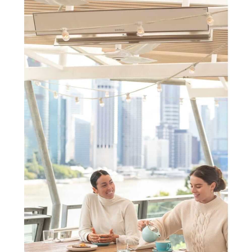 Bromic Platinum Smart-Heat Electric Heater warming an outdoor cafe setting with city skyline backdrop.