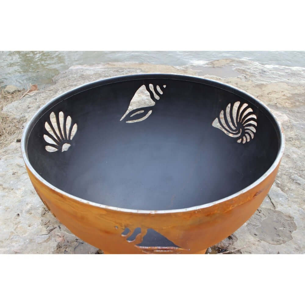 Fire Pit Art Beachcomber 36-Inch Handcrafted Carbon Steel Gas Fire Pit -Decorative metal bowl with shell designs on a stone surface