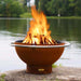 Fire Pit Art Bella Luna 48-Inch Handcrafted Carbon Steel Fire Pit (BL) - Fire pit with flames burning in a natural setting by a body of water.