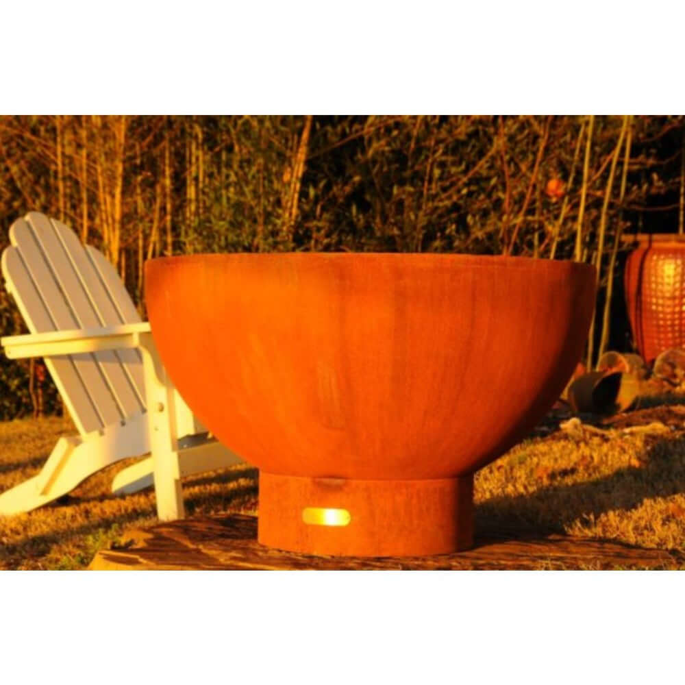 Fire Pit Art Crater 36-Inch Handcrafted Carbon Steel Fire Pit (CTR) - Rust-colored fire pit in a garden setting with a white chair and lantern.