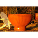 Fire Pit Art Crater 36-Inch Handcrafted Carbon Steel Fire Pit (CTR) - Rust-colored fire pit in a garden setting with a white chair and lantern.