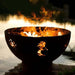 Fire Pit Art Kokopelli 36-Inch Handcrafted Carbon Steel Fire Pit (KO) - Fire pit with flames burning in it, placed by a body of water.
