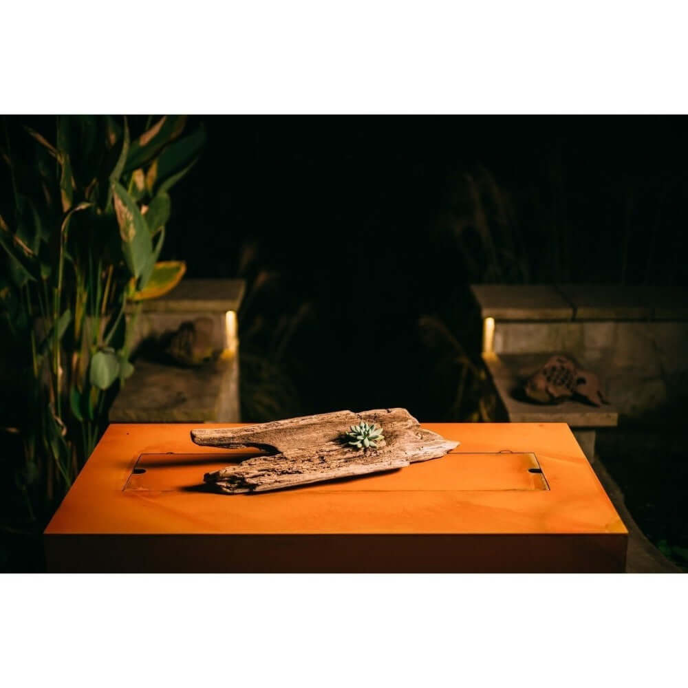 Fire Pit Art Linear 36-Inch Handcrafted Carbon Steel Gas Fire Pit - Wooden tray with a small plant on an orange surface, blurred background