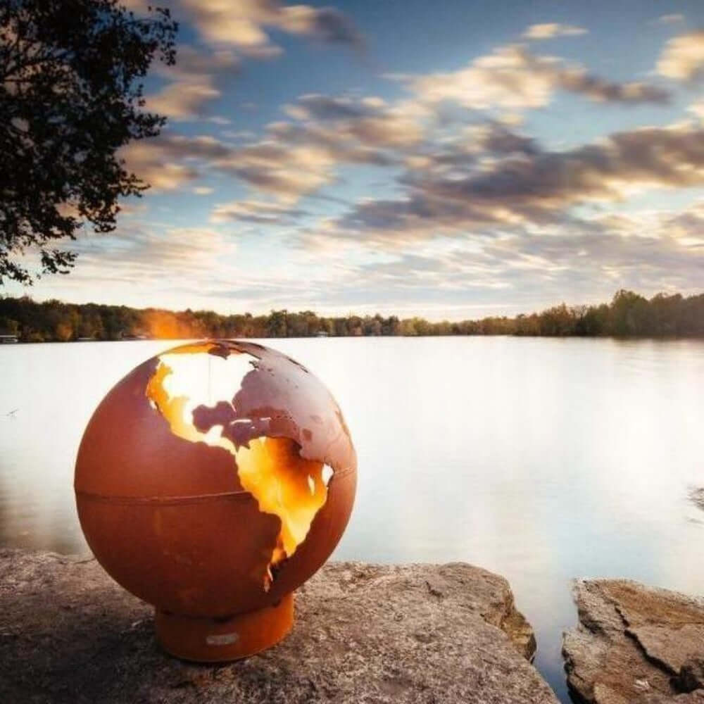 Fire Pit Art Third Rock Globe Shaped 36-Inch Carbon Steel Fire Pit (TR) - Globular fire pit on a rock by a lake with a sunset sky