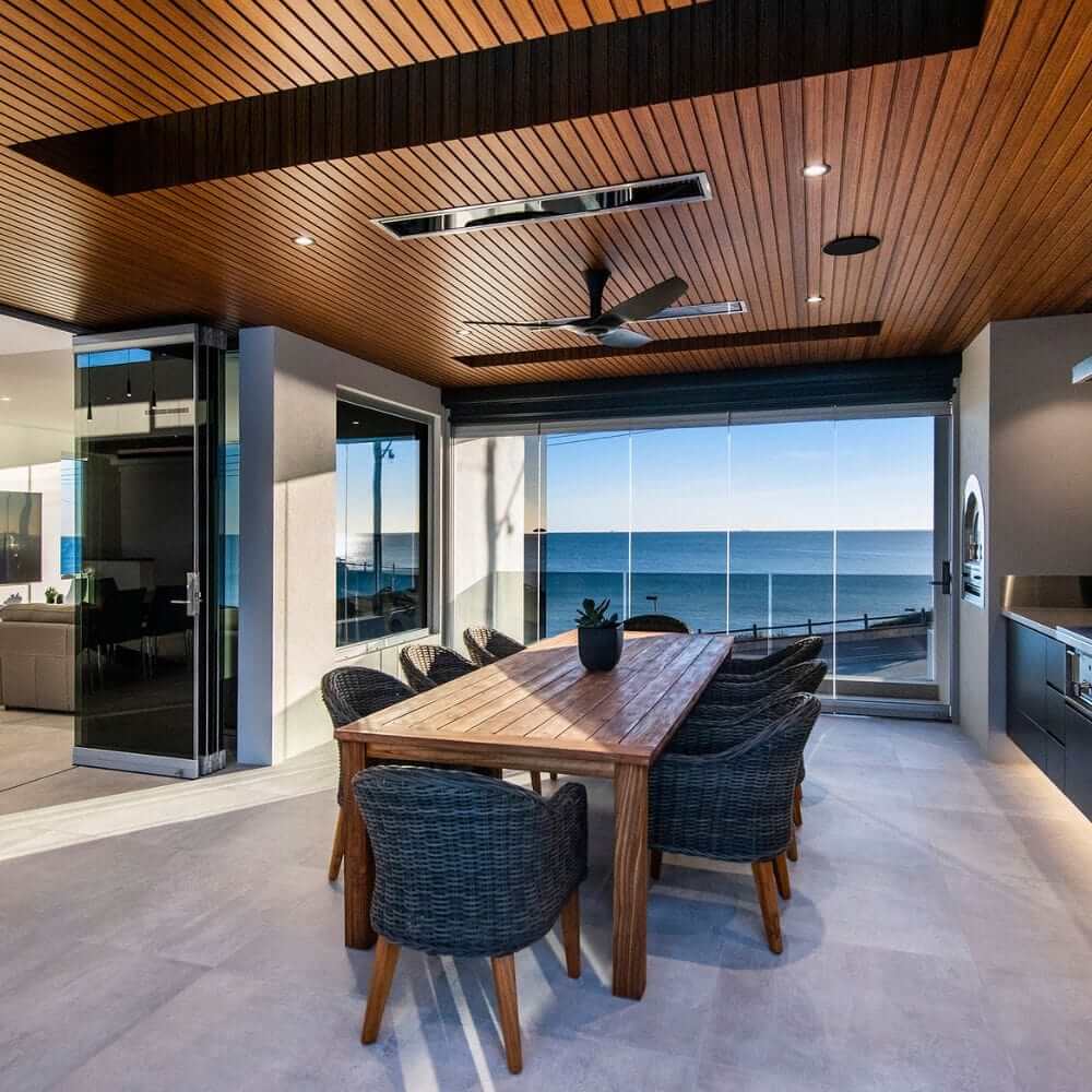 Stylish outdoor dining area with a wooden table and views of the ocean through large windows.