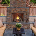 Outdoor natural gas fireplace with stone surround and flames, surrounded by cozy seating and greenery.