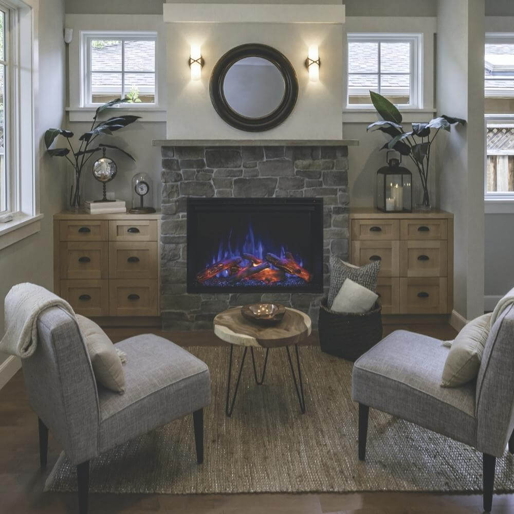Redstone 26" Built-in Electric Fireplace Insert - Cozy living area featuring a stone fireplace with blue flames, two gray chairs, a wooden coffee table, and indoor plants.