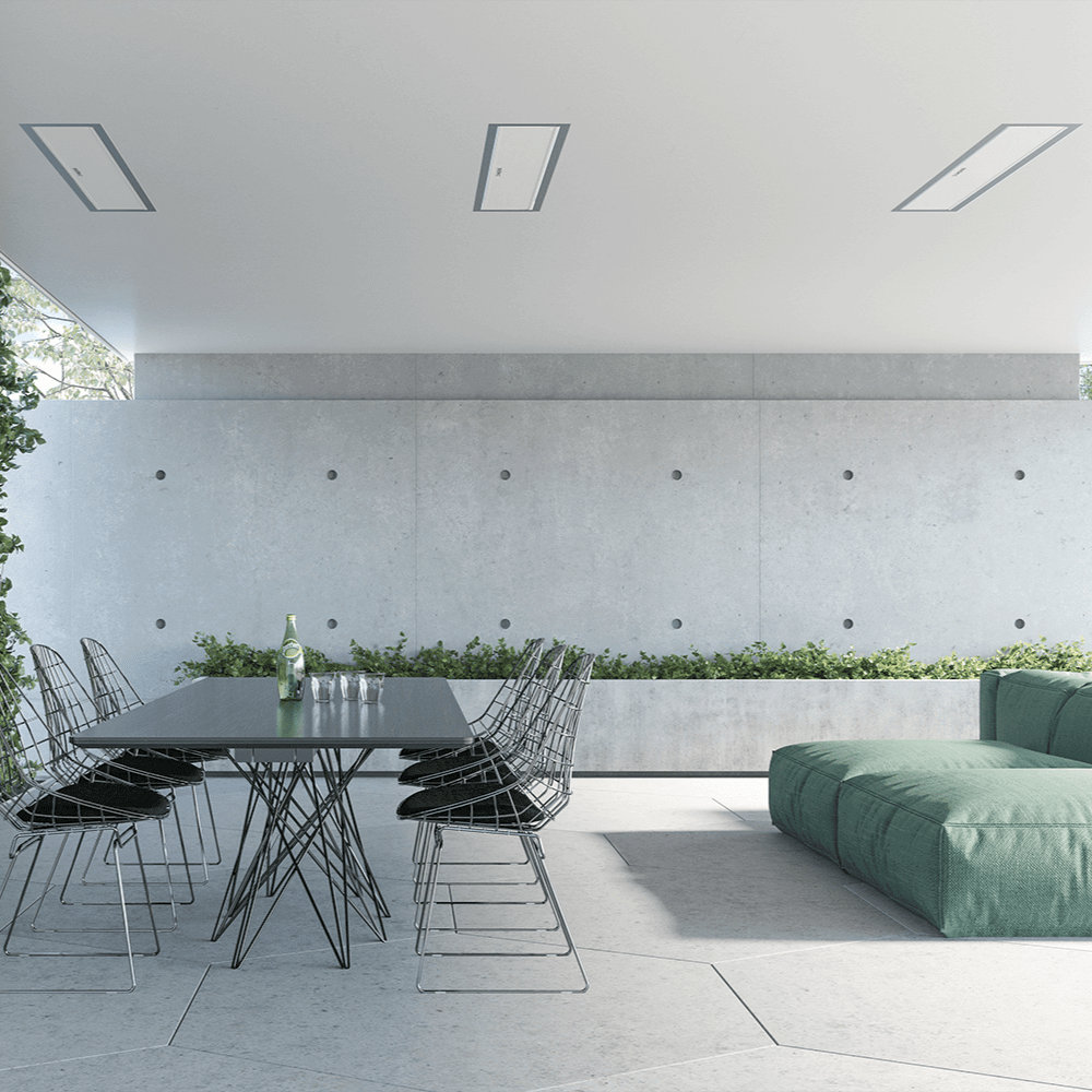 Modern outdoor dining area with a sleek table, wire chairs, and green couch surrounded by greenery.