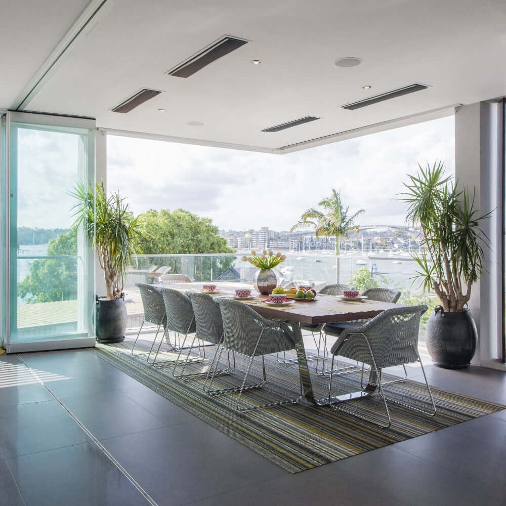 Modern outdoor dining area with wall-mounted heaters and scenic waterfront view.