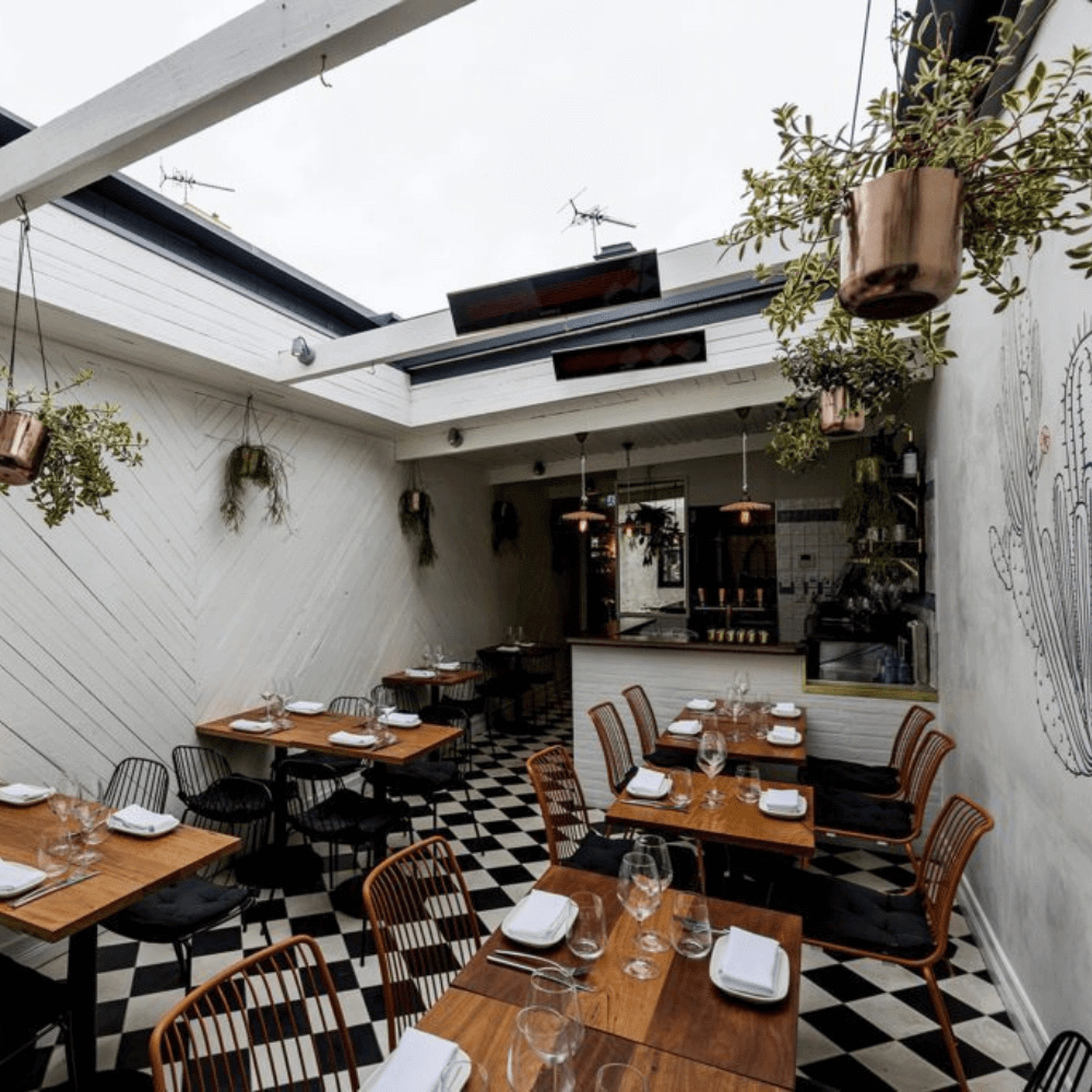 Stylish restaurant interior featuring wooden tables, checkered floor, and hanging plants for a cozy dining atmosphere.