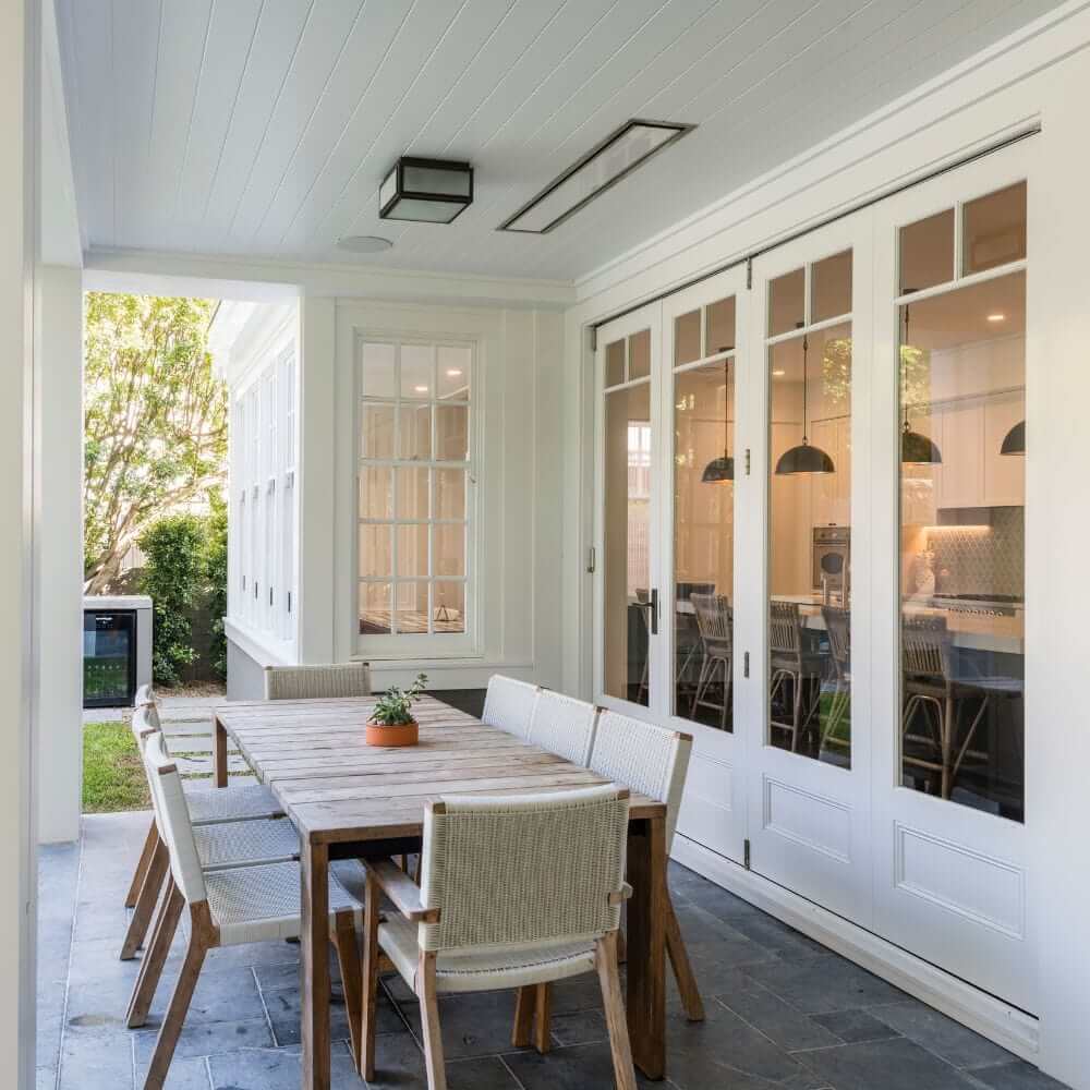 Modern outdoor dining area with a wooden table and chairs, featuring large windows and sleek decor.