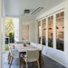 Modern outdoor dining area with a wooden table and chairs, featuring large windows and sleek decor.