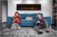 Amantii Symmetry Lumina Electric Fireplace - Two people sitting on a blue couch with a dog, using smartphones, in a living room setting.