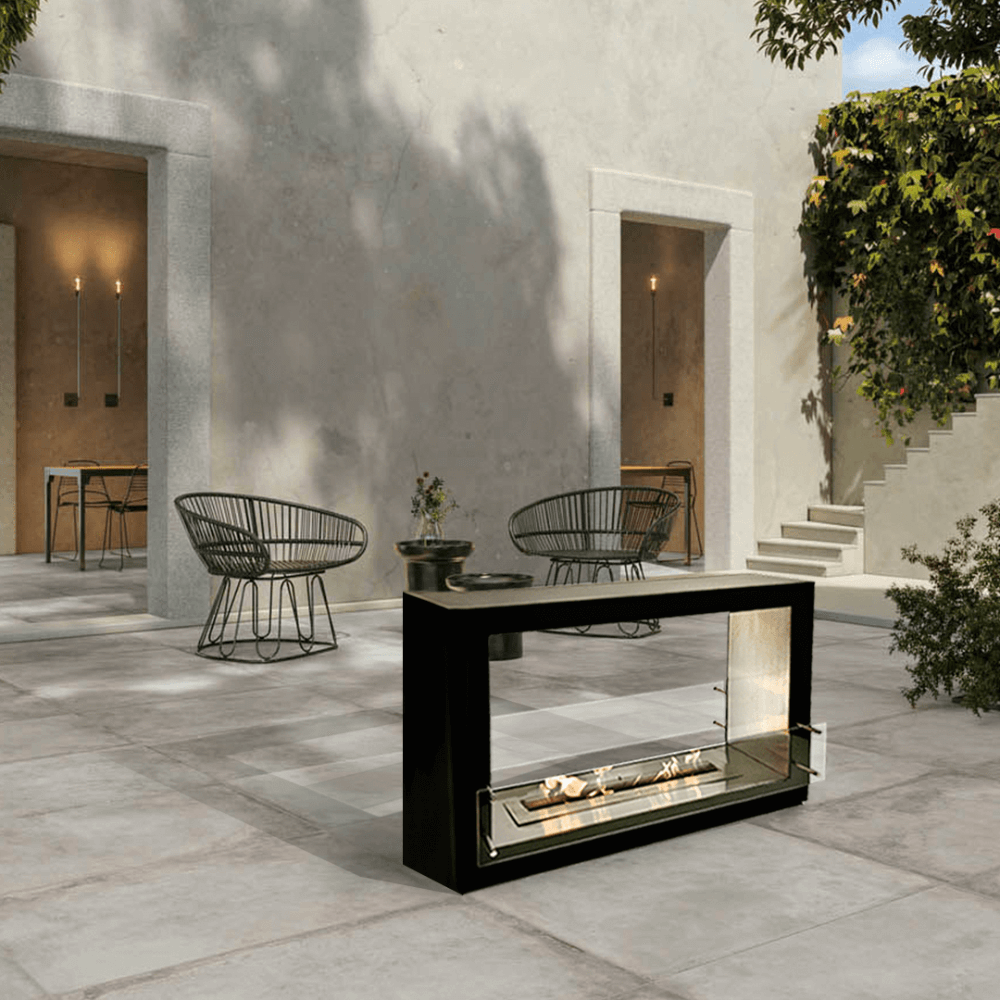 The Bio Flame Sek XL 53-Inch Free Standing See-Through Ethanol Fireplace - A sleek modern outdoor fireplace surrounded by a cozy courtyard